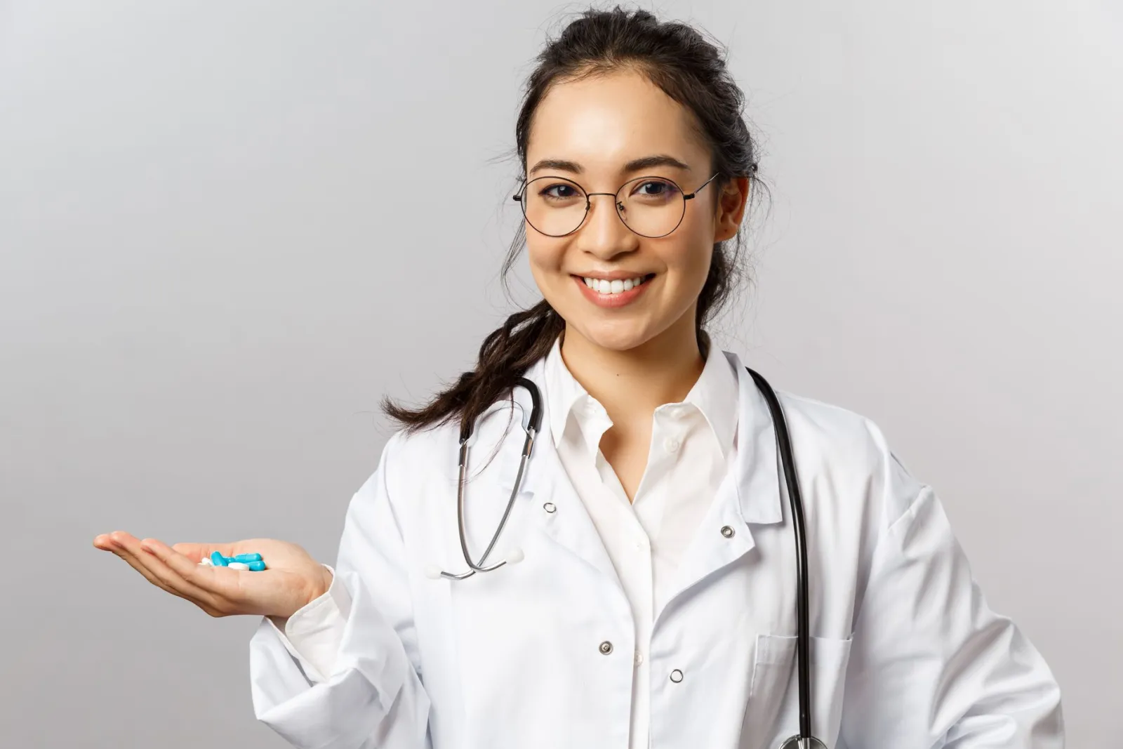 Asian female doctor smiling while holding pills. Promoting healthcare and medicine.